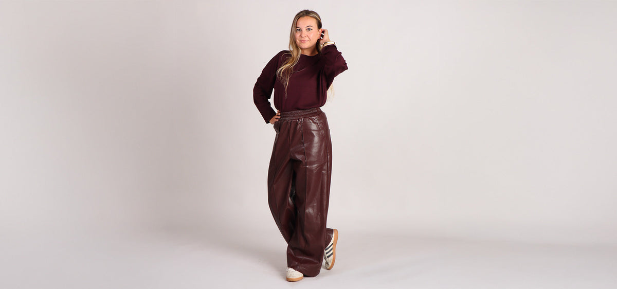 Model draagt bordeauxrode knit en vegan leather bordeaux rode broek. De perfecte herfst/winter look van 2025/2026.